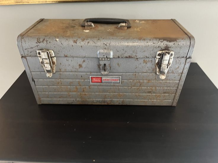 an old metal tool box sitting on top of a black table next to a painting