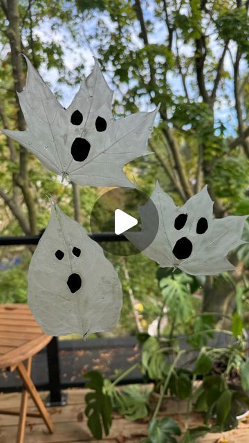 three white leaves hanging from the side of a window with black dots on them, in front of some trees