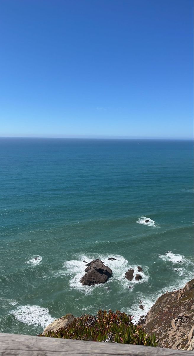 the ocean is blue with waves coming in from the shore and rocks on the beach