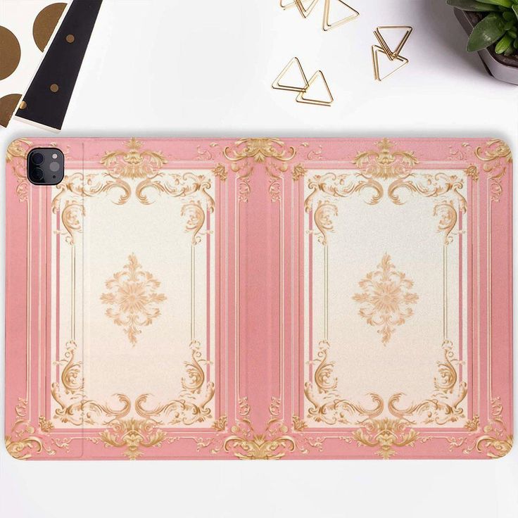 a pink and gold phone case sitting on top of a desk next to a plant