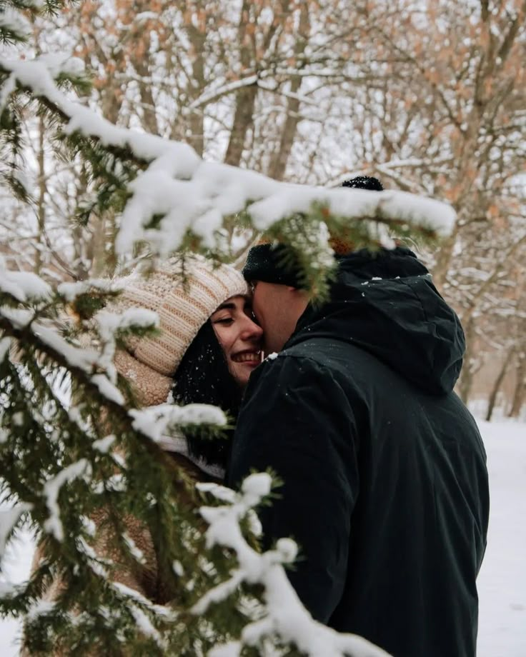 a man and woman standing next to each other in front of trees covered with snow