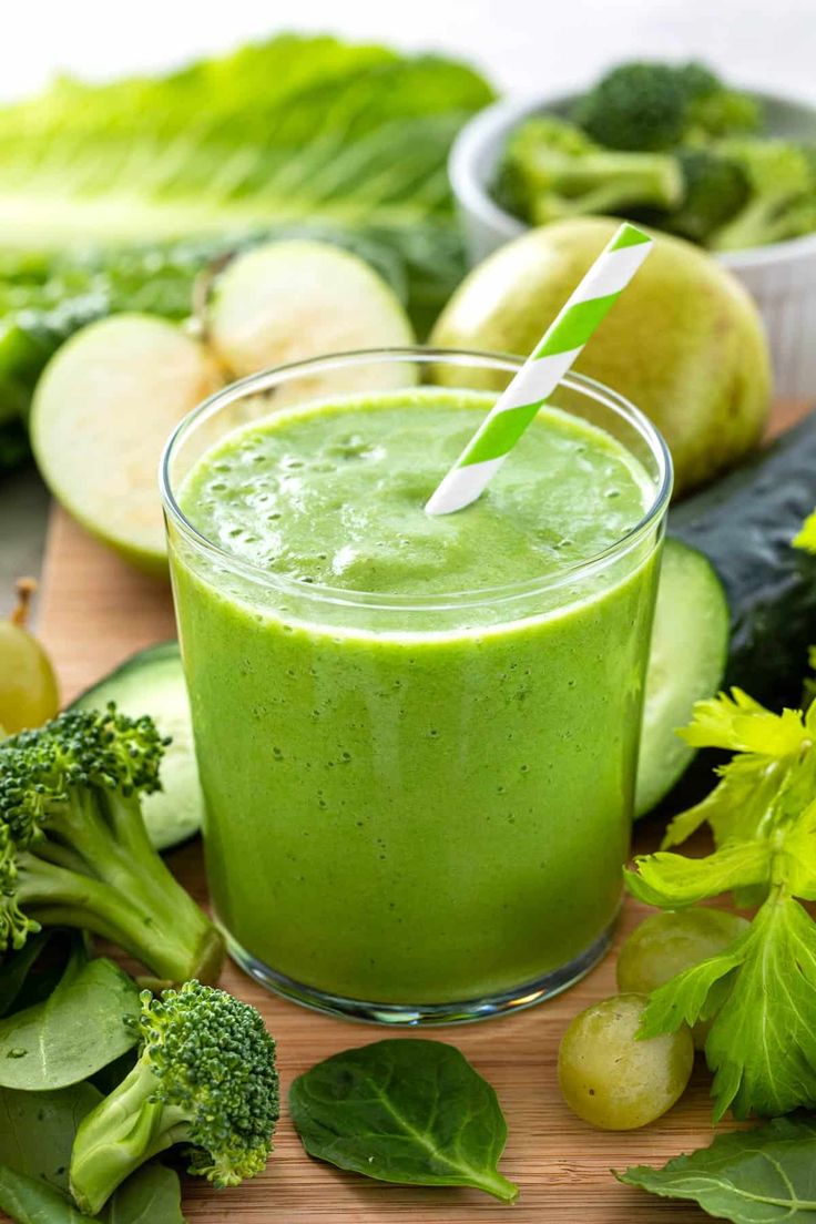 a green smoothie in a glass surrounded by vegetables