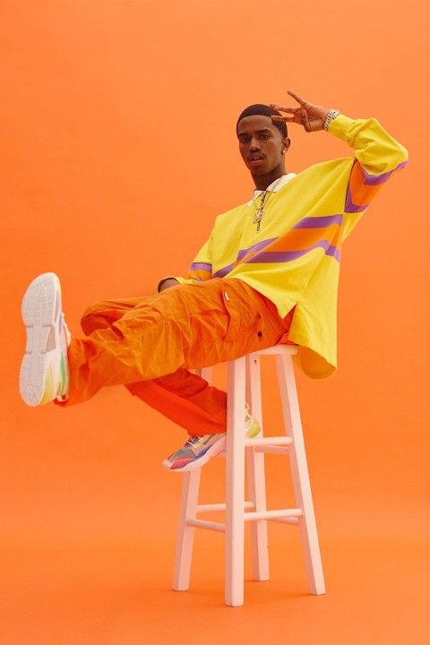 a man sitting on top of a white stool wearing an orange and yellow outfit with his feet up