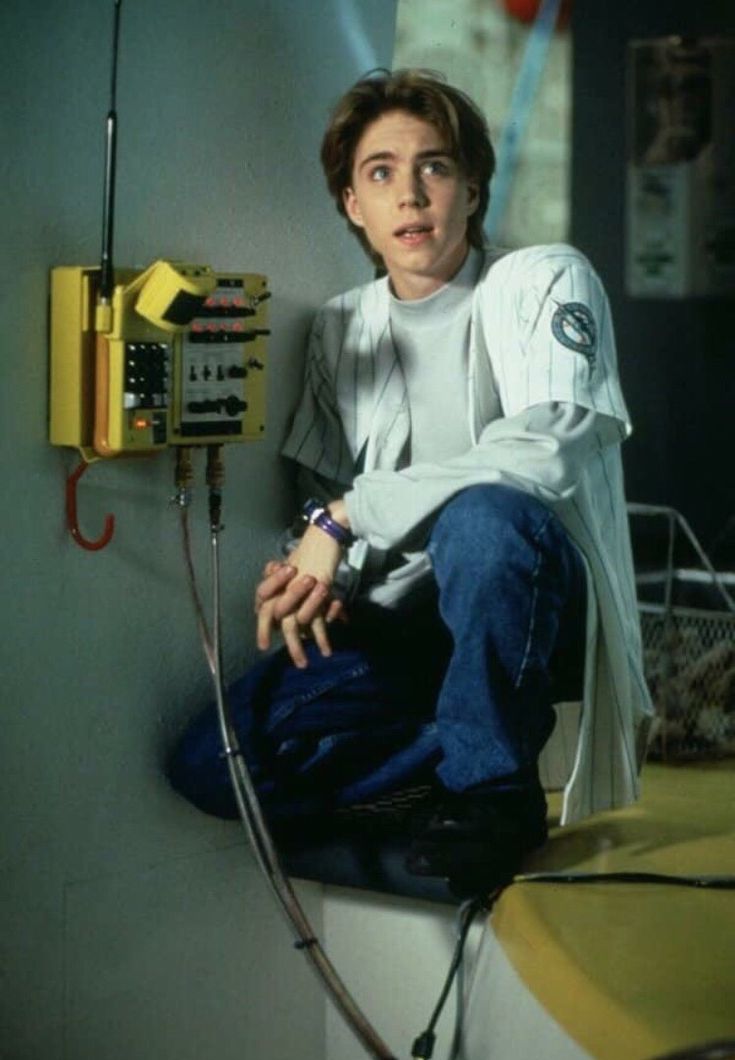 a young man sitting on top of a toilet next to a yellow phone and wires