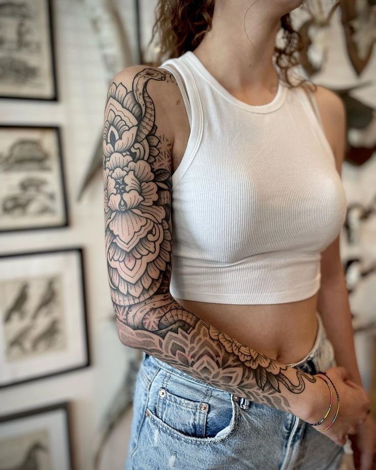 a woman with tattoos on her arms and chest standing in front of a wall full of pictures