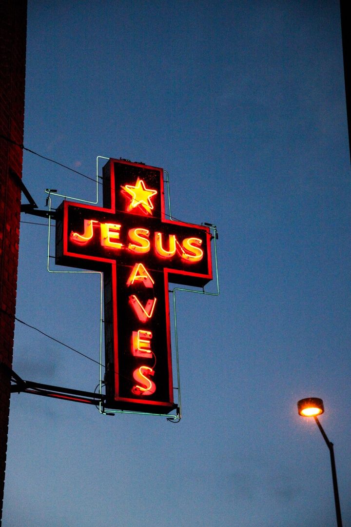 a neon sign that says jesus saves hangs from the side of a building in front of a street light