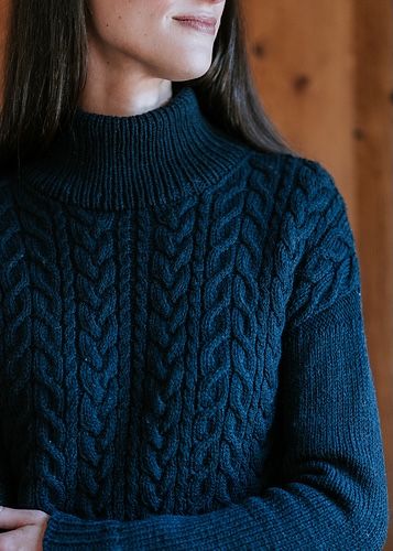 a woman with long hair wearing a blue cable knit sweater looking off to the side