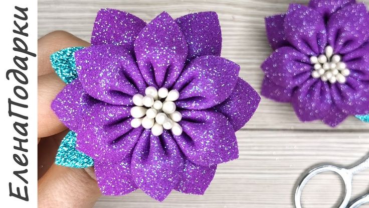 two purple flowers with white center being held by someone's hand next to scissors