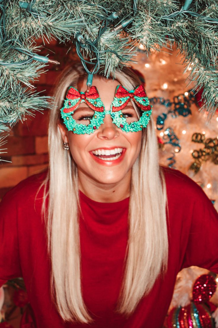 a woman with long blonde hair wearing green and red eye masks in front of a christmas tree