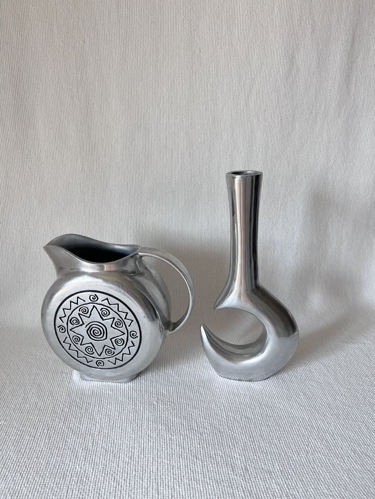 two silver vases sitting next to each other on a white surface