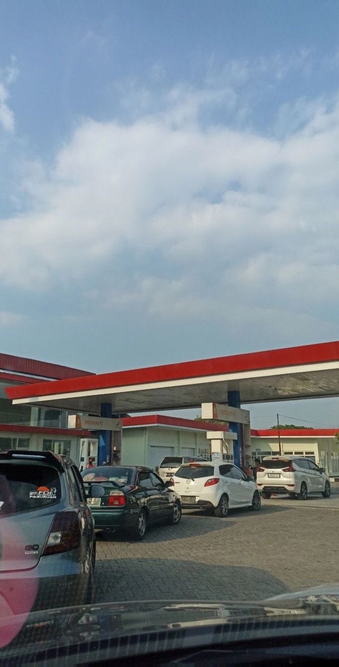 cars parked in front of a gas station under a blue sky with some white clouds