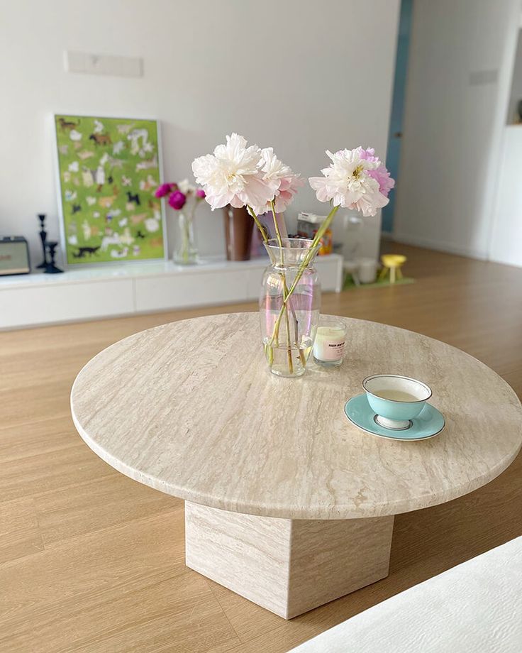 a table with flowers in a vase on it and a cup next to the coffee table