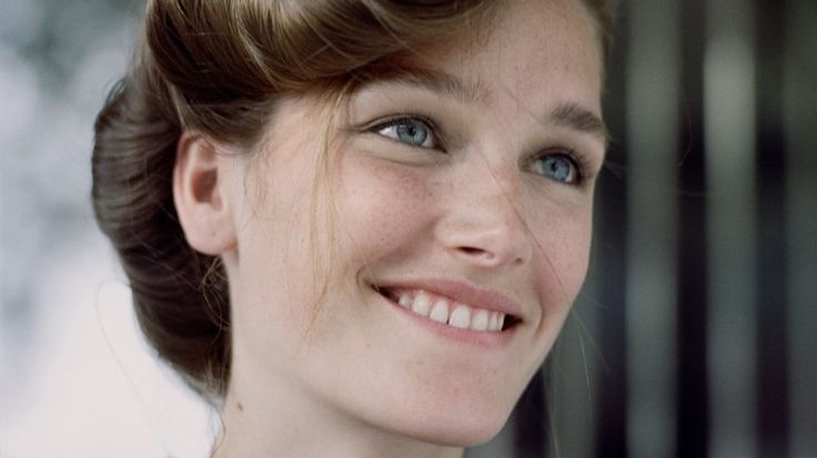 a close up of a woman with blue eyes and a bun in her hair smiling at the camera