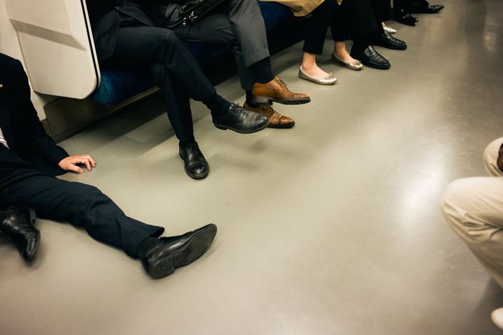 a group of people sitting next to each other on a subway train with their feet up