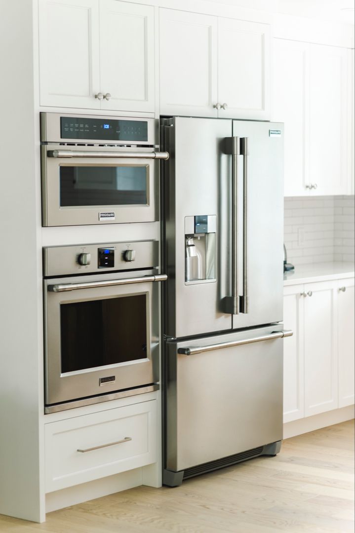 a stainless steel refrigerator and oven in a white kitchen with wood floors, cabinets and drawers