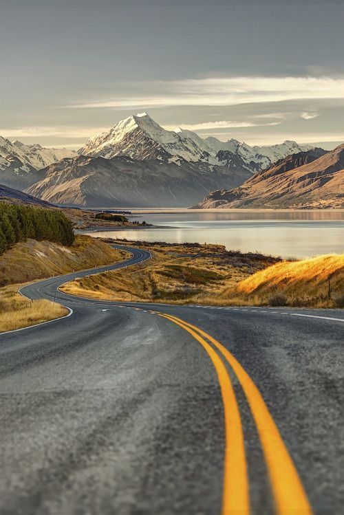 an empty road in the middle of nowhere with mountains in the background and water on either side