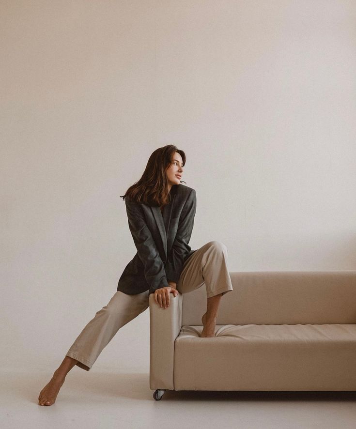 a woman sitting on top of a couch in front of a white wall with her legs crossed