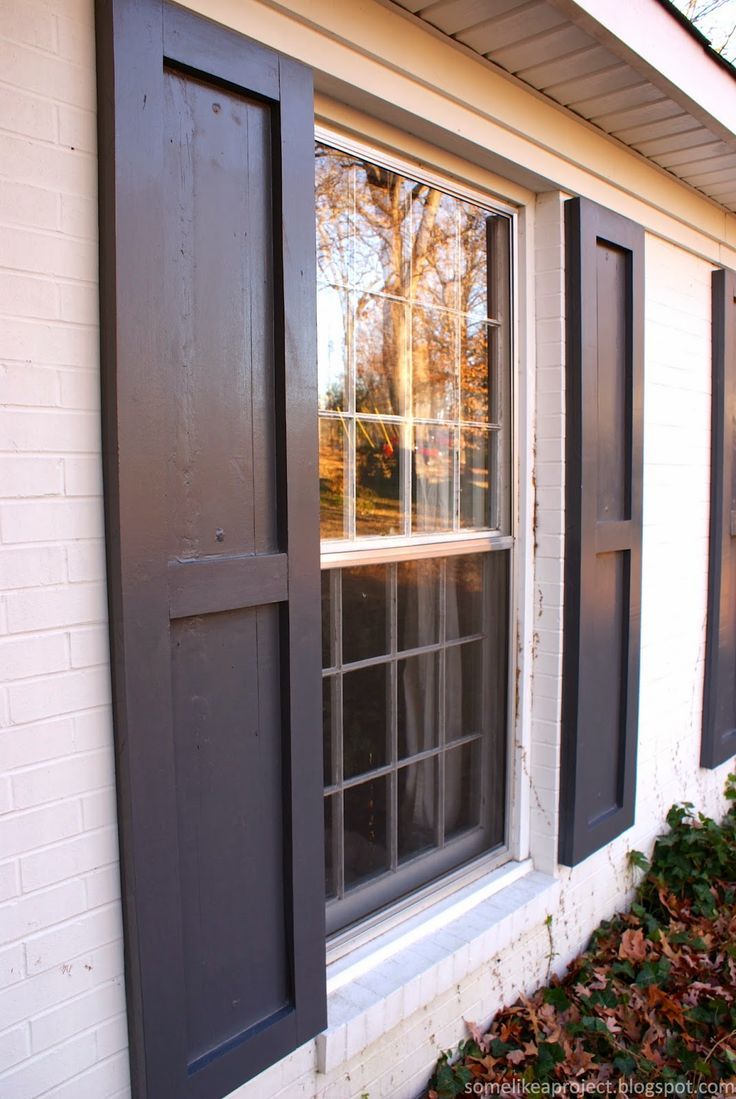 an open window on the side of a white brick building with black shutters and wood trim