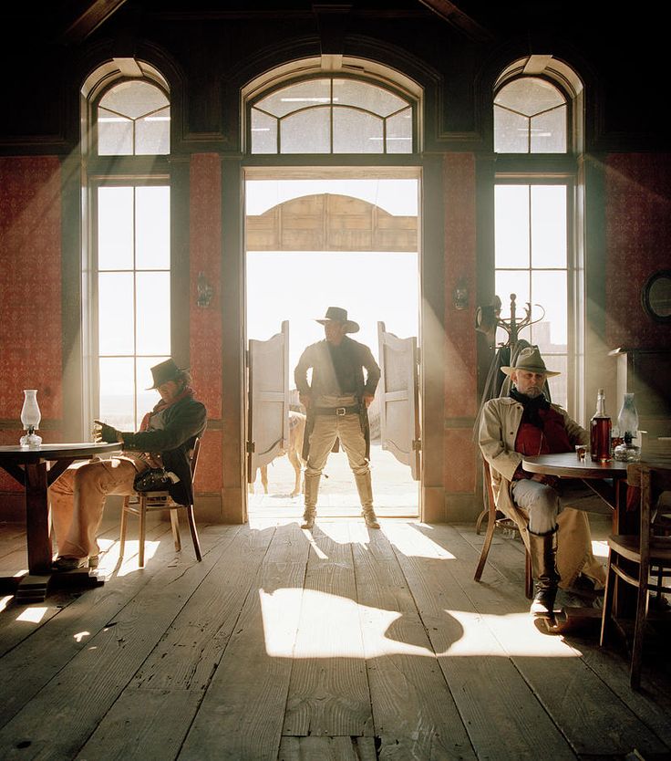 two men in period clothing sitting at desks and looking out large windows with sunlight streaming through them