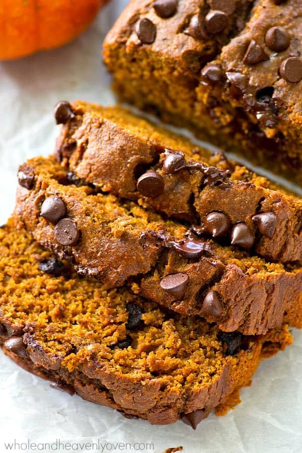 two slices of chocolate chip pumpkin bread on top of parchment paper with an orange in the background