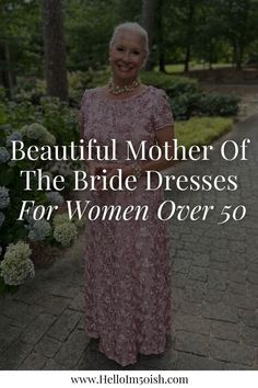 an older woman in a pink dress standing on a path with trees and flowers behind her