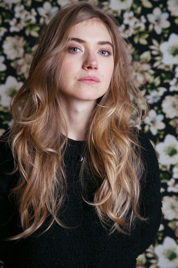 a woman with long blonde hair standing in front of a floral wallpapered background