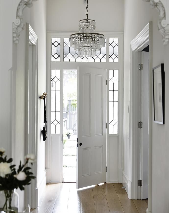 an entry way with white doors and chandelier hanging from the ceiling, surrounded by wood flooring