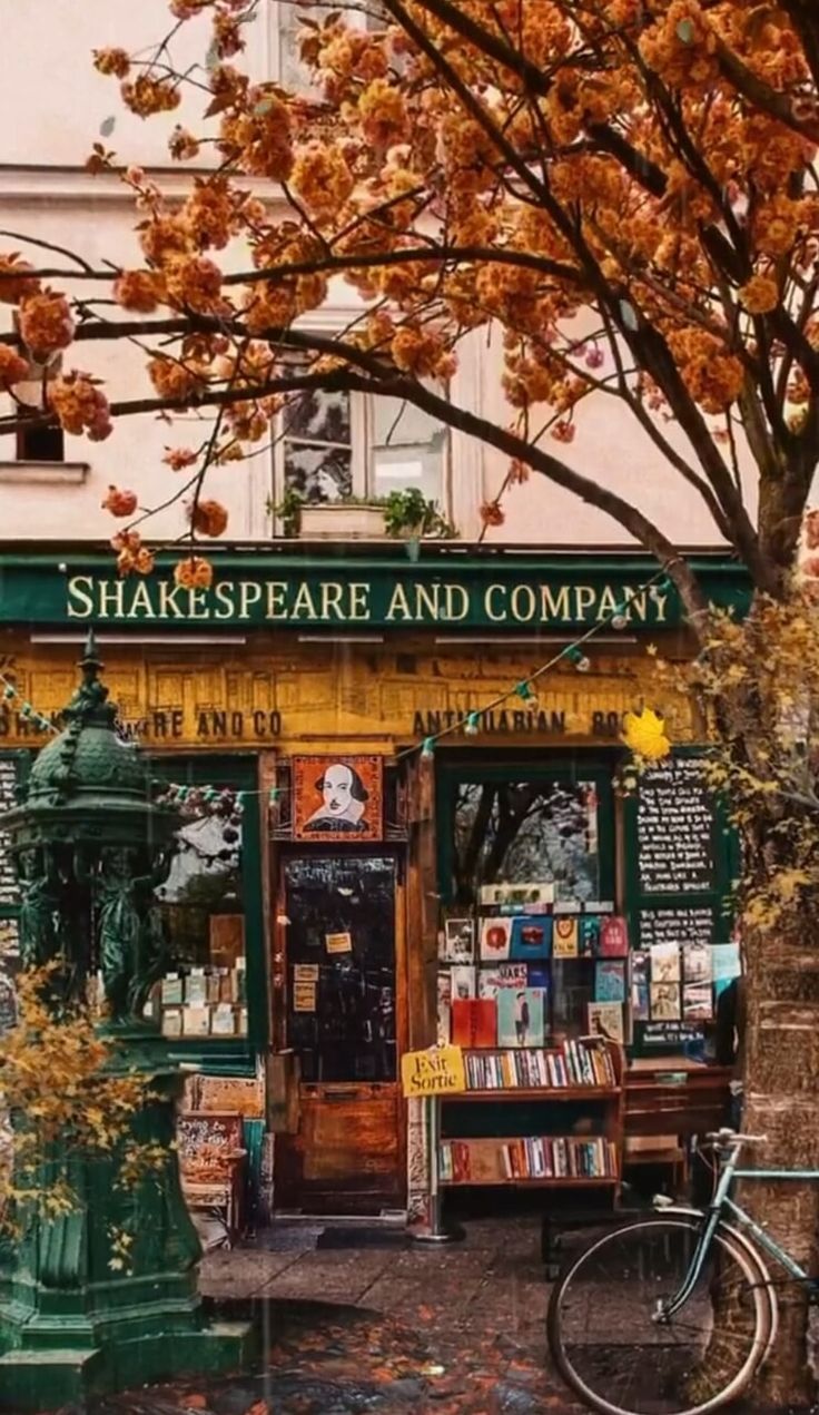 a bike parked in front of a book store with pink flowers on the tree branches