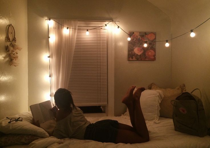 a woman laying in bed reading a book with fairy lights on the wall behind her