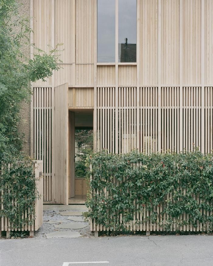 an entrance to a building with wooden slats on the side and green plants growing in front