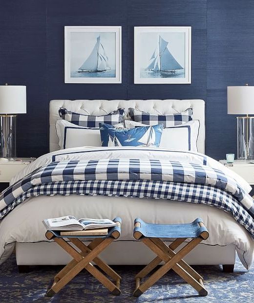 a blue and white bedroom with two pictures on the wall above the bed, along with an upholstered bench