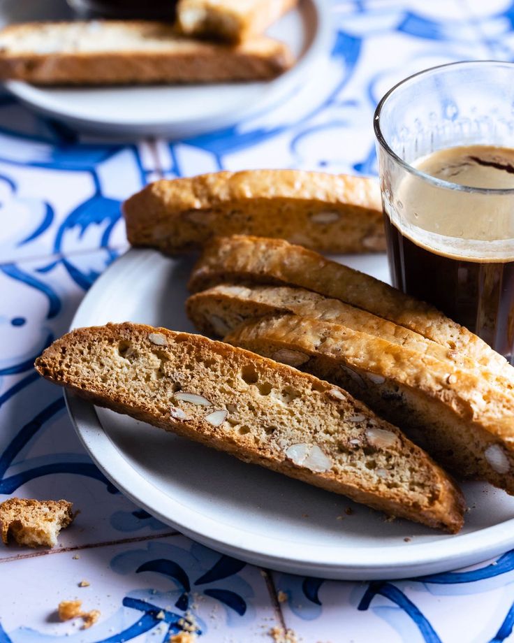 some bread sticks are on a plate and next to a cup of coffee with something in it