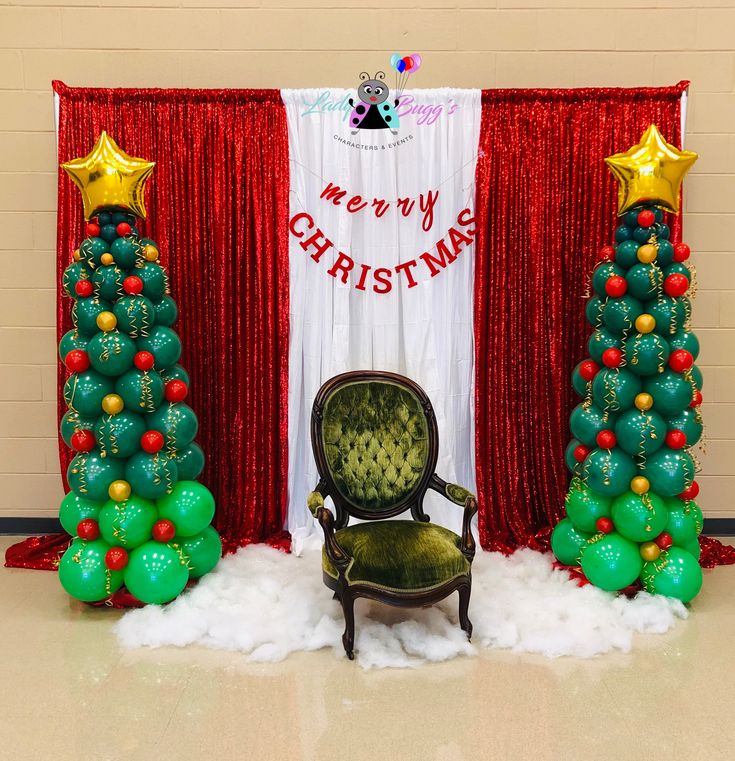 a chair sitting in front of a christmas tree with balloons on the floor and red curtains behind it