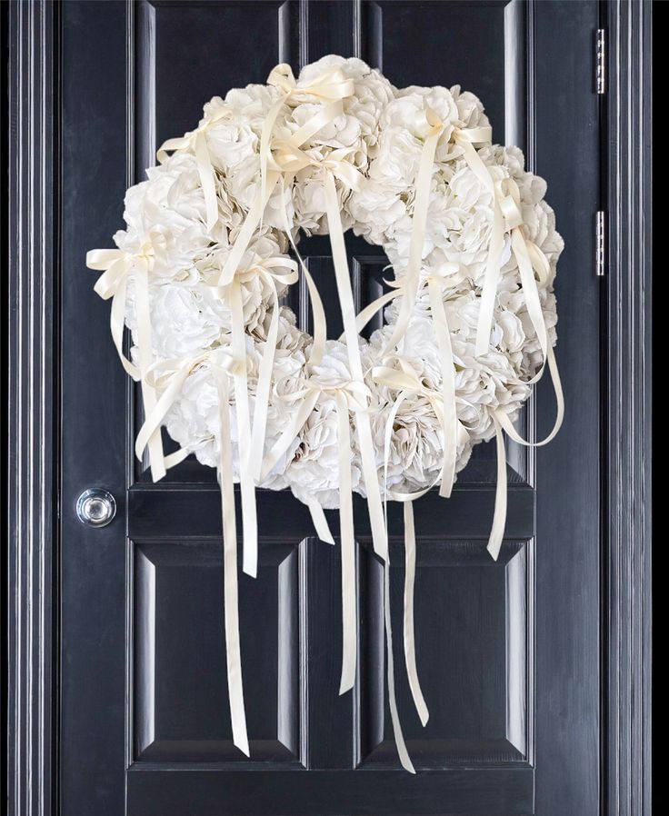 a wreath made out of white flowers hangs on the front door's black door