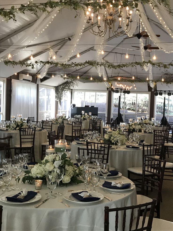 a banquet hall with tables and chairs covered in white linens, decorated with greenery