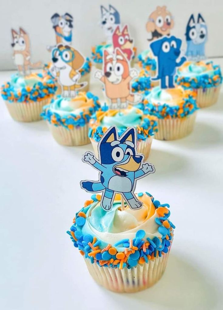 cupcakes with blue frosting and cartoon characters on them are arranged in rows