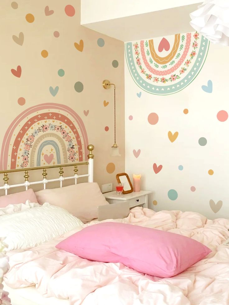 a white bed topped with pink pillows next to a wall covered in rainbows and hearts