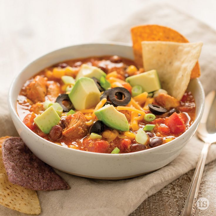 a bowl of chili with tortilla chips and avocado