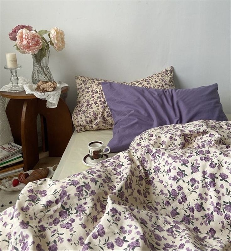 a bed covered in purple and white flowers next to a night stand with two candles on it