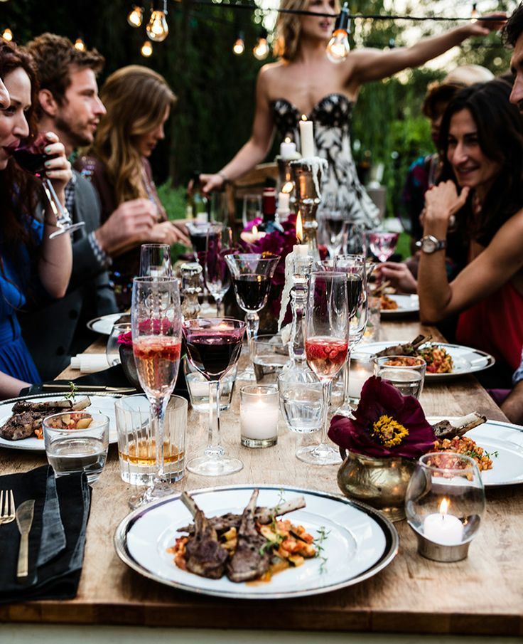 a group of people sitting around a table with food and wine glasses on top of it