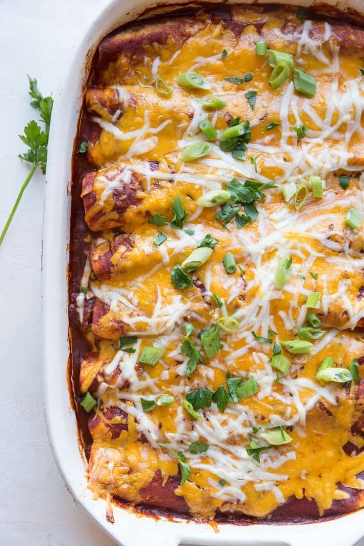 an enchilada casserole in a white dish with cheese and green garnish