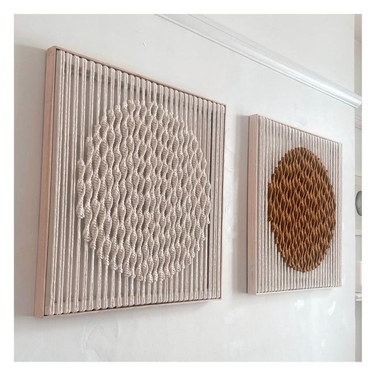 two wall hangings on the side of a white wall, one with a woven circle