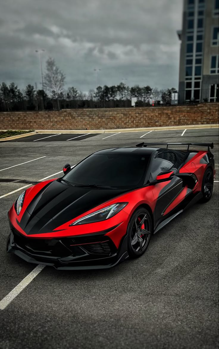 a red and black sports car parked in a parking lot next to a tall building