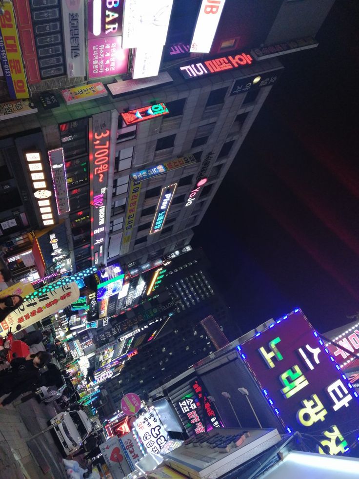 a city street filled with lots of neon signs and buildings at night in the distance