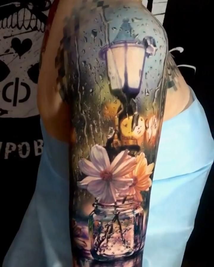 a person with a tattoo on their arm holding a jar full of flowers and a lamp