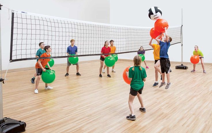 a group of people playing volleyball on a hard wood floor with balls in the air