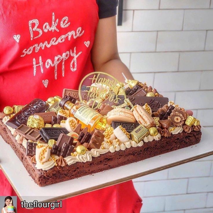 a person in an apron holding a cake with chocolates and candy on it that says bake someone happy