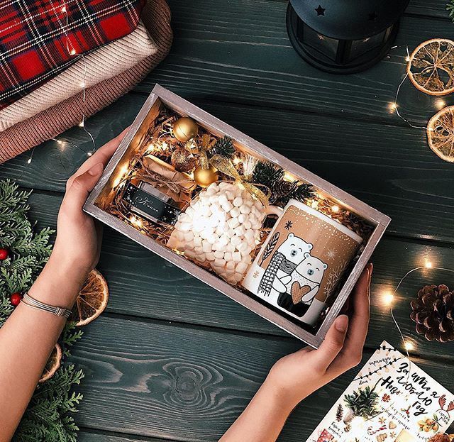 a person holding a box filled with christmas items on top of a wooden table next to other holiday decorations