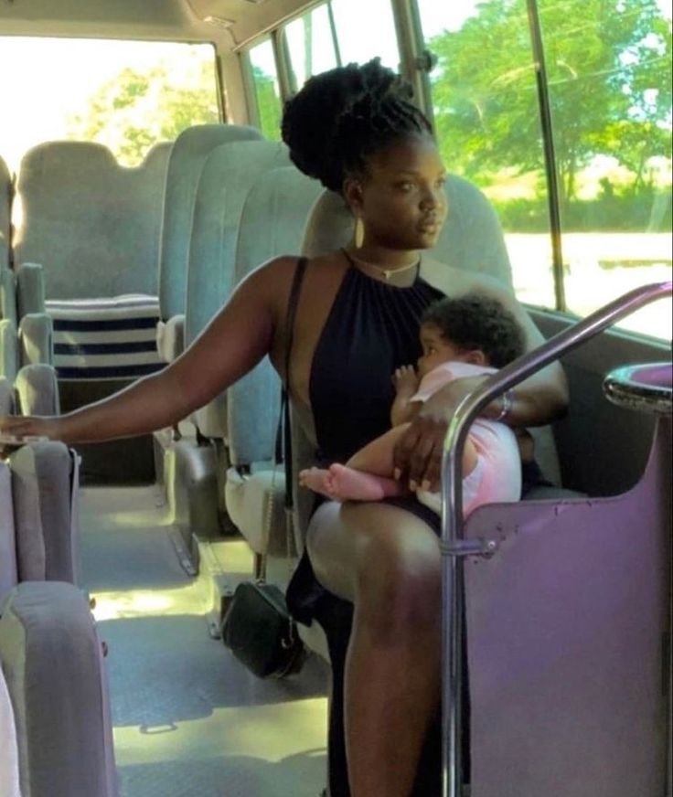 a woman sitting in the back of a bus holding a baby and wearing a black dress