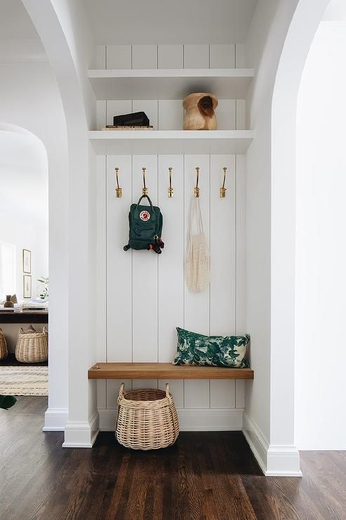 an entryway with white walls and wood flooring has a wooden bench, green purse, and hanging hooks on the wall